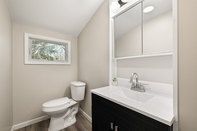 half bathroom featuring wood finished floors, toilet, vanity, baseboards, and lofted ceiling