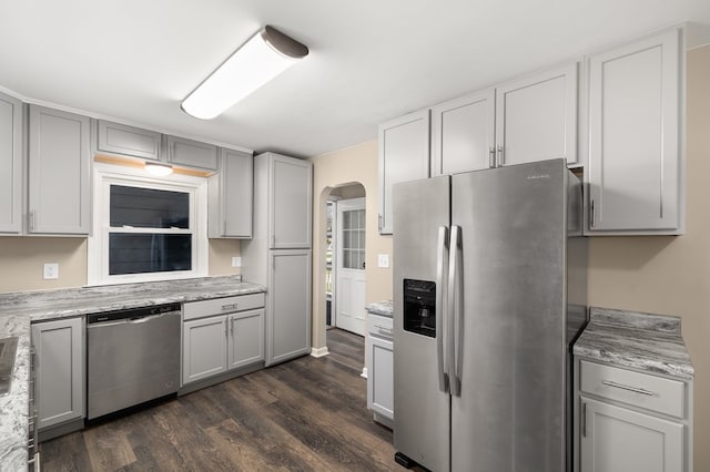 kitchen featuring arched walkways, light stone counters, appliances with stainless steel finishes, dark wood-style flooring, and gray cabinetry