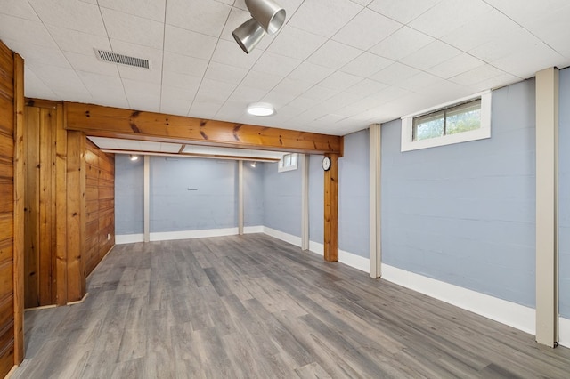 basement with baseboards, visible vents, wood finished floors, and wood walls