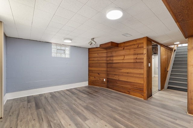 below grade area with concrete block wall, stairway, wood finished floors, and baseboards