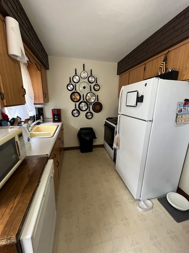 kitchen featuring brick wall, white appliances, and sink