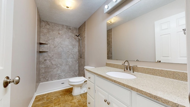 full bathroom with a tile shower, toilet, vanity, and a textured ceiling