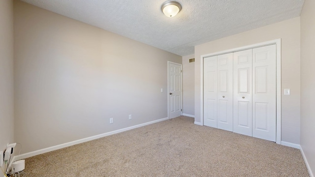 unfurnished bedroom with a closet, a textured ceiling, visible vents, carpet, and baseboards