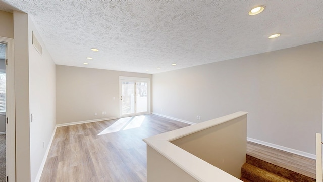 spare room featuring a textured ceiling, baseboards, light wood finished floors, and recessed lighting