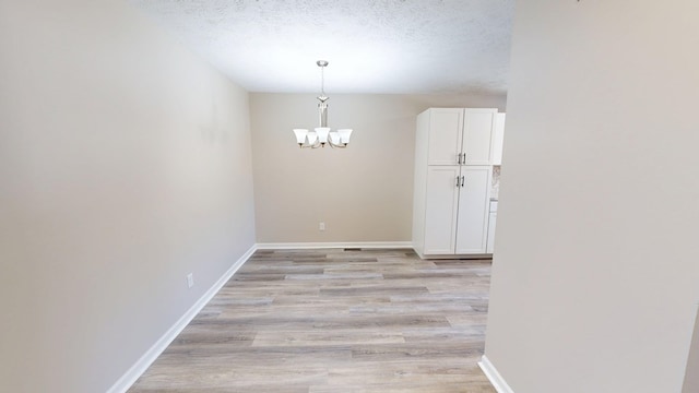 unfurnished dining area featuring baseboards, a textured ceiling, a chandelier, and light wood-type flooring