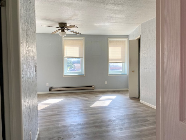 spare room with ceiling fan, light wood-type flooring, baseboard heating, and a wealth of natural light