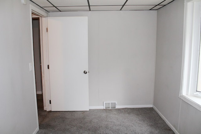 spare room featuring a paneled ceiling and dark carpet