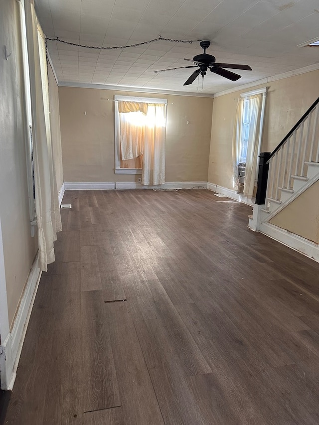 unfurnished living room with a ceiling fan, wood finished floors, crown molding, baseboards, and stairs