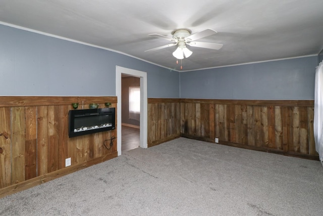 carpeted spare room featuring ceiling fan, crown molding, and wooden walls