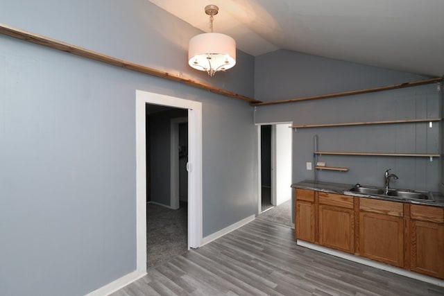 kitchen featuring vaulted ceiling, sink, wood-type flooring, and decorative light fixtures