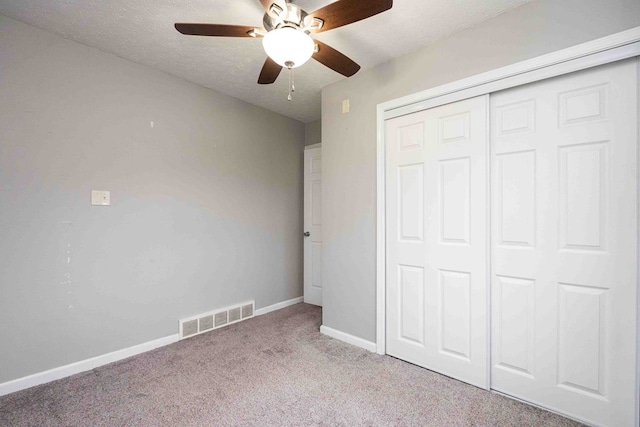 unfurnished bedroom featuring ceiling fan, a closet, light colored carpet, and a textured ceiling