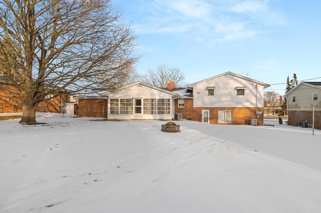 snow covered property with a fire pit and a sunroom