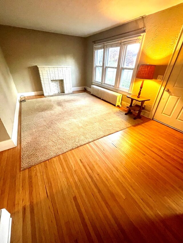 242 Davis Rd, Mansfield, OH 44907 - unfurnished living room featuring baseboards, radiator heating unit, wood finished floors, and a fireplace