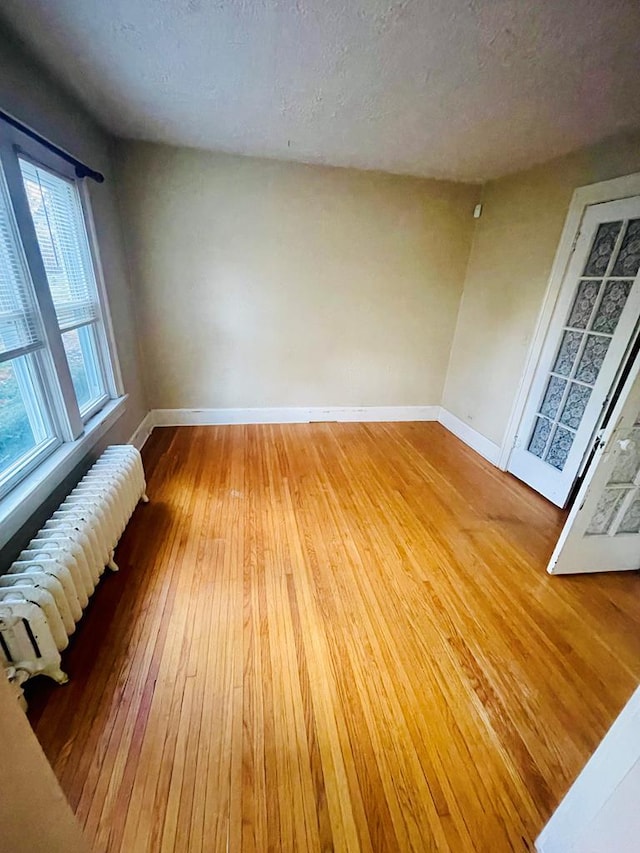242 Davis Rd, Mansfield, OH 44907 - unfurnished room with radiator heating unit, baseboards, a textured ceiling, and light wood-style floors