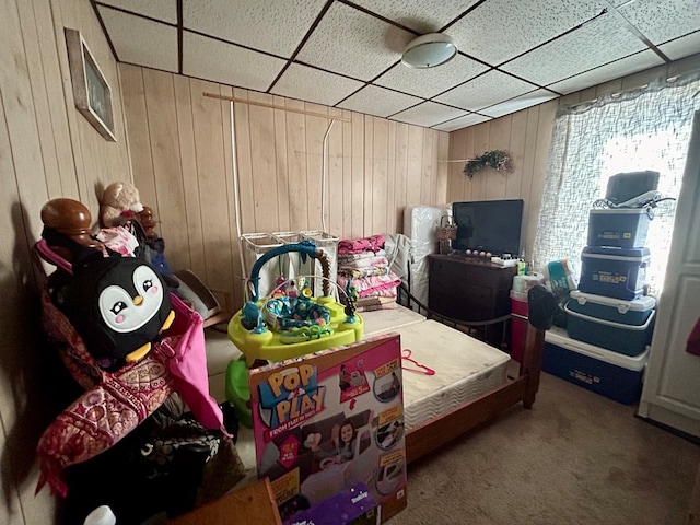 bedroom with carpet floors, a drop ceiling, and wooden walls