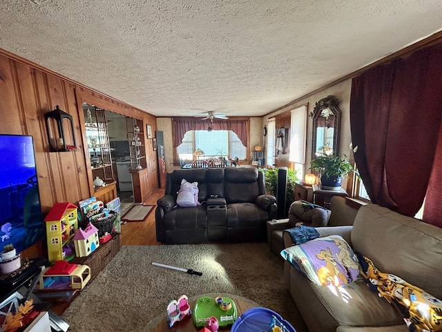 living room featuring a textured ceiling, ceiling fan, ornamental molding, and wood walls