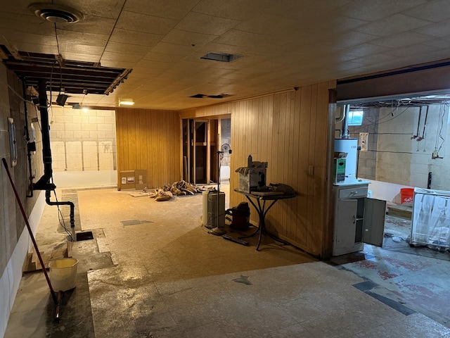 unfinished basement featuring gas water heater, wooden walls, concrete block wall, and tile patterned floors