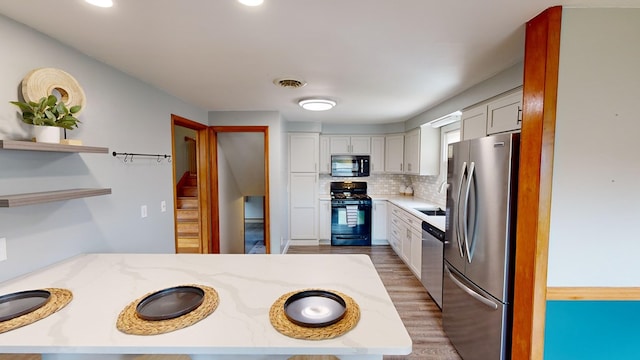 kitchen featuring light stone countertops, sink, decorative backsplash, white cabinets, and black appliances