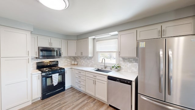 kitchen with white cabinetry, sink, backsplash, appliances with stainless steel finishes, and light wood-type flooring