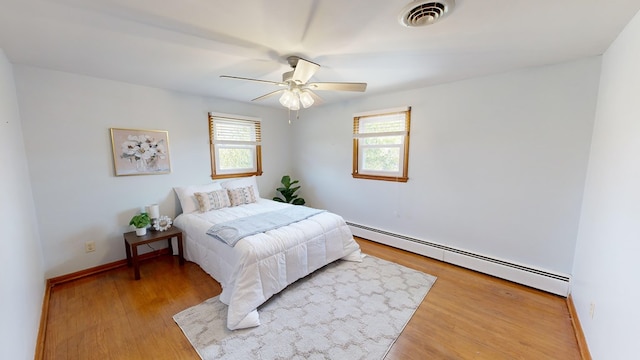 bedroom with ceiling fan, hardwood / wood-style flooring, and a baseboard heating unit