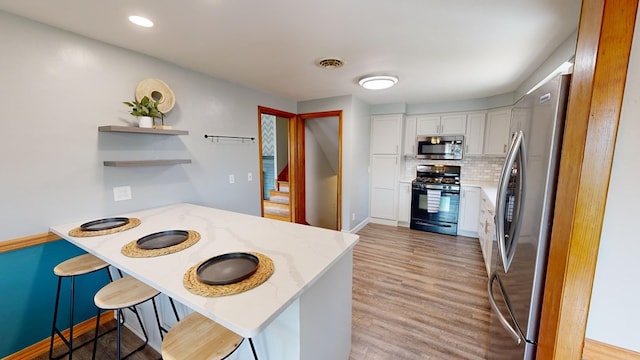 kitchen with white cabinets, appliances with stainless steel finishes, tasteful backsplash, light stone counters, and kitchen peninsula