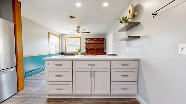 kitchen with dark wood-type flooring, white cabinets, ceiling fan, baseboard heating, and stainless steel refrigerator