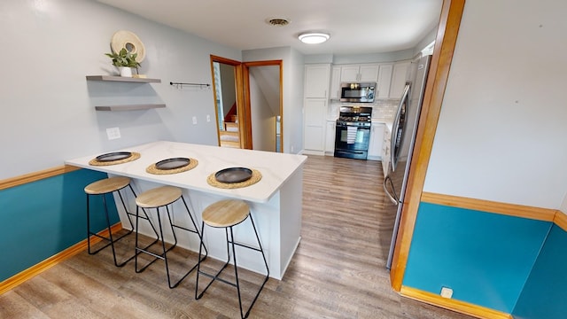 kitchen with a kitchen breakfast bar, white cabinetry, light hardwood / wood-style floors, and appliances with stainless steel finishes