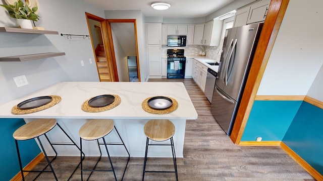 kitchen featuring light stone counters, a breakfast bar area, decorative backsplash, appliances with stainless steel finishes, and light wood-type flooring