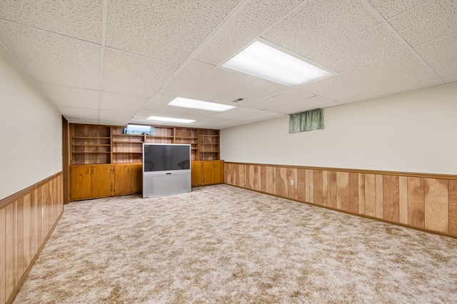 basement with light carpet, built in features, and a drop ceiling