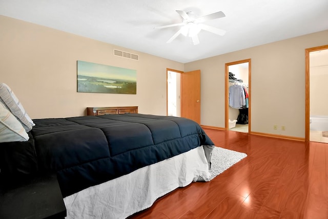 bedroom with ensuite bathroom, a walk in closet, ceiling fan, wood-type flooring, and a closet