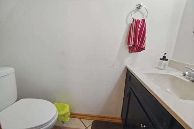 half bathroom featuring toilet, tile patterned floors, baseboards, and vanity