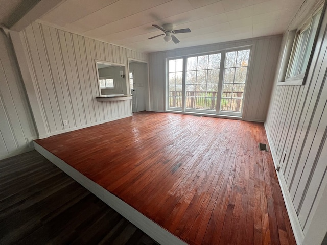 unfurnished room featuring ceiling fan, wood-type flooring, and wooden walls