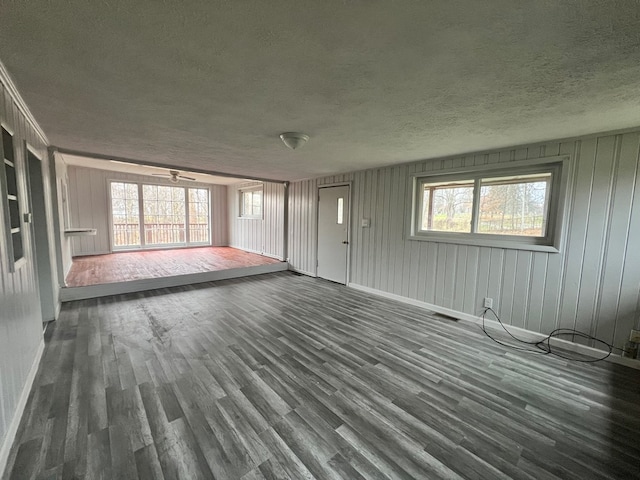 unfurnished living room with a wealth of natural light, dark wood-type flooring, and a textured ceiling