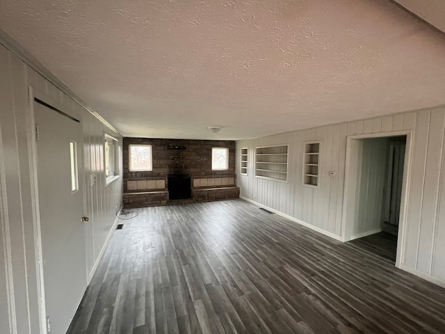 unfurnished living room featuring a fireplace, built in shelves, a textured ceiling, and dark wood-type flooring