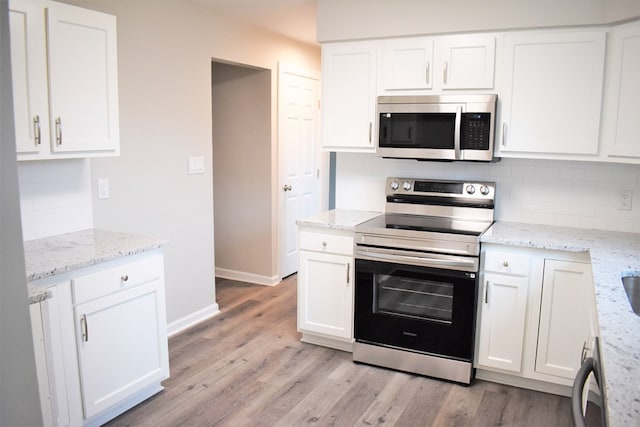 kitchen with tasteful backsplash, light stone counters, light hardwood / wood-style flooring, white cabinets, and appliances with stainless steel finishes