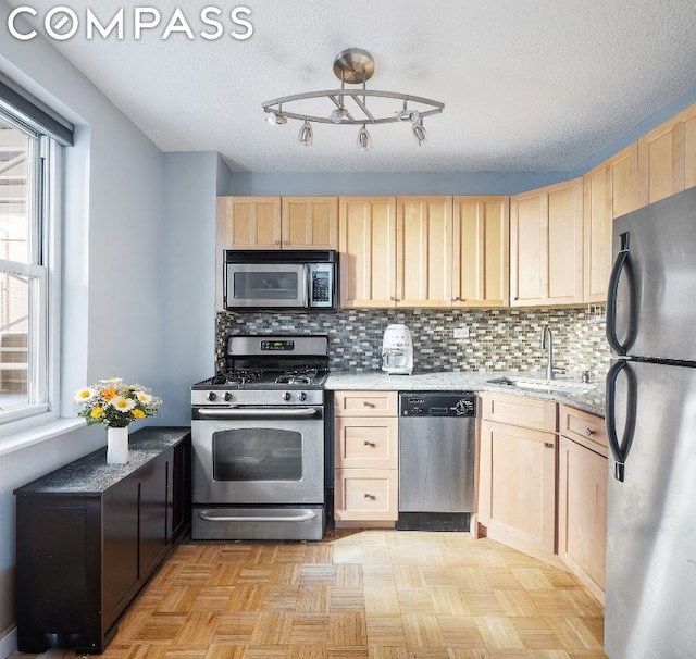 kitchen with a textured ceiling, light brown cabinets, stainless steel appliances, sink, and backsplash