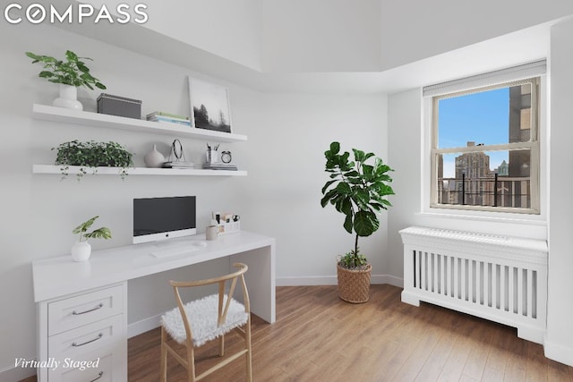 home office featuring built in desk, wood-type flooring, and radiator heating unit