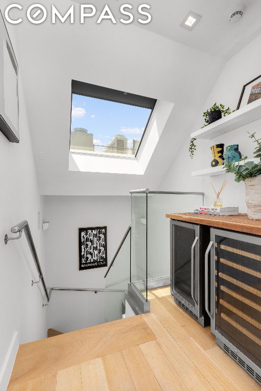 stairs with hardwood / wood-style floors, beverage cooler, and lofted ceiling