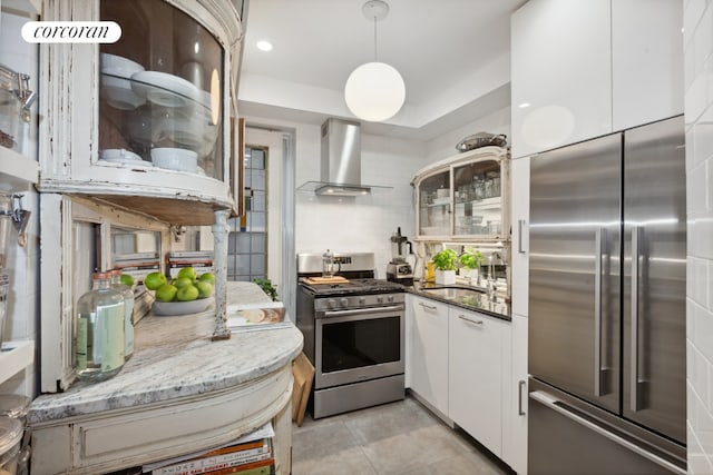 kitchen with decorative backsplash, dark stone counters, appliances with stainless steel finishes, wall chimney range hood, and white cabinetry