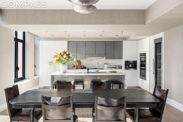 kitchen with a kitchen bar, sink, white cabinetry, and hardwood / wood-style flooring