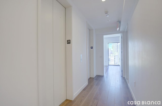 hallway featuring baseboards, light wood finished floors, and elevator