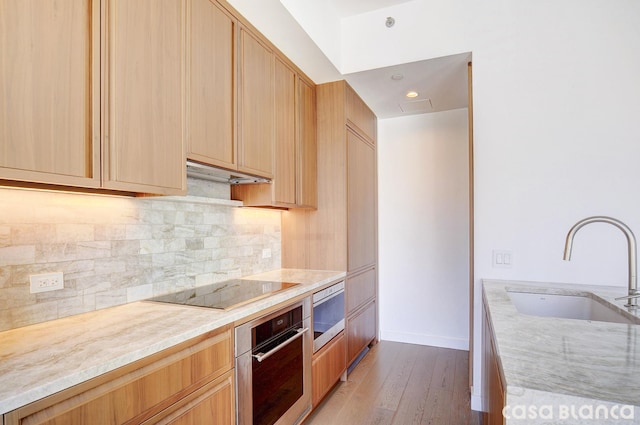 kitchen with light stone countertops, black electric stovetop, under cabinet range hood, stainless steel oven, and a sink