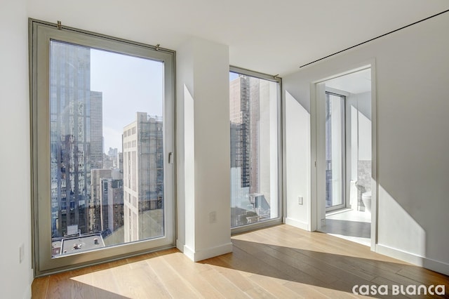 doorway to outside featuring a wall of windows, a city view, baseboards, and wood finished floors