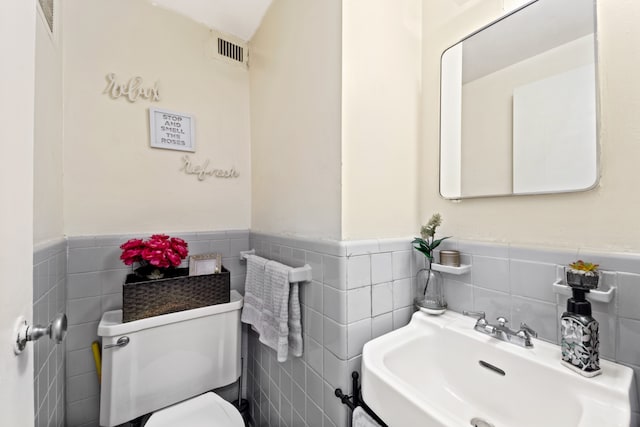 half bath featuring toilet, a wainscoted wall, a sink, and visible vents