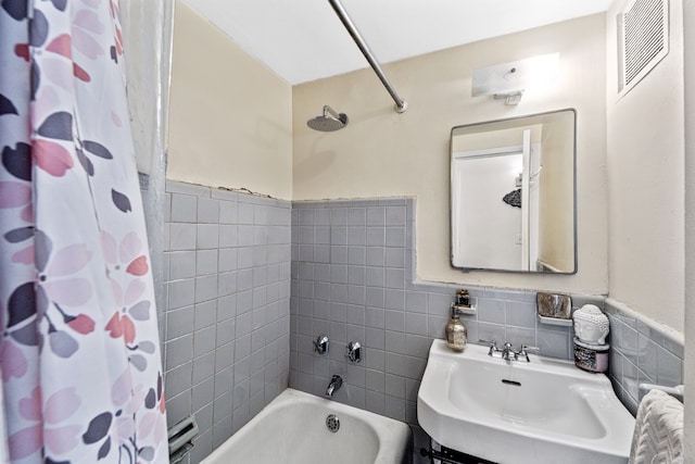 bathroom featuring a sink, visible vents, tile walls, wainscoting, and shower / bathtub combination with curtain