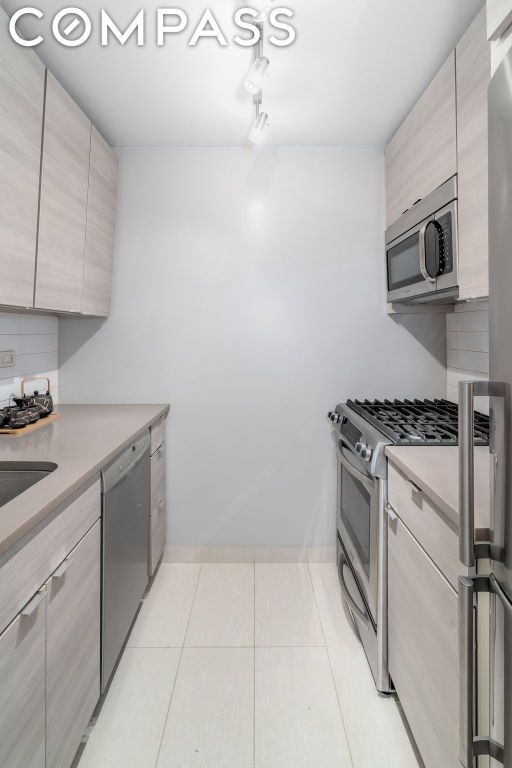 kitchen featuring light tile patterned floors, decorative backsplash, light brown cabinetry, and stainless steel appliances