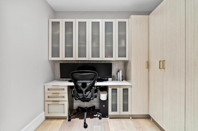 home office featuring baseboards, built in desk, and light wood finished floors