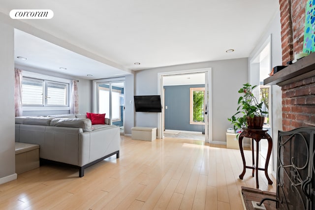 living room with a healthy amount of sunlight, a brick fireplace, and light hardwood / wood-style floors