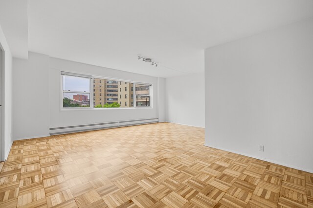 unfurnished room with a baseboard radiator, light parquet flooring, and track lighting