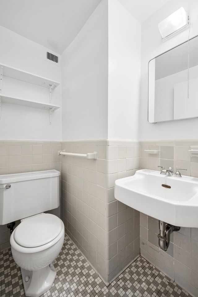 bathroom with visible vents, toilet, a wainscoted wall, tile patterned flooring, and tile walls